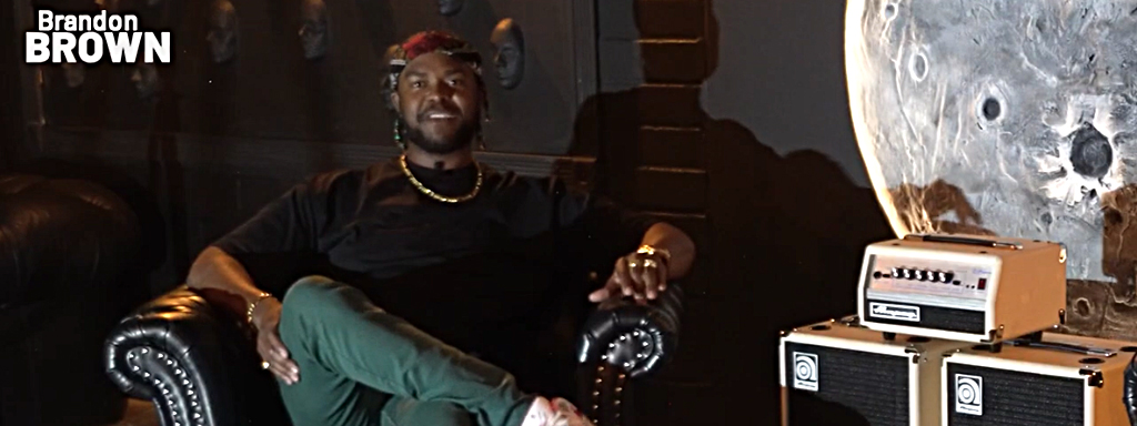 Screenshot from video with Brandon Brown sitting on chair by Ampeg Micro head and cab
